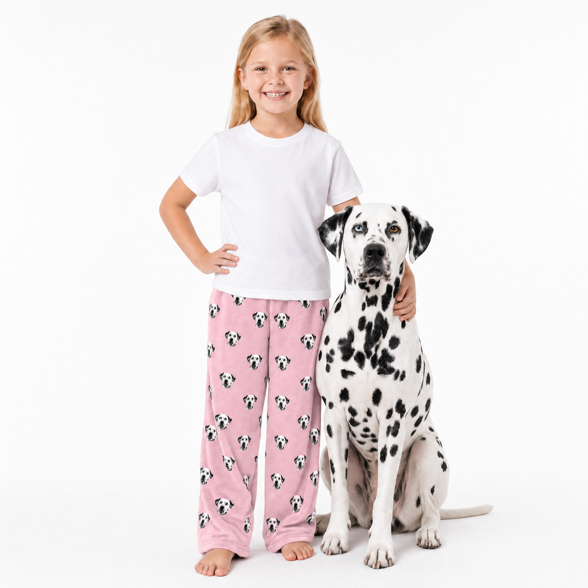 Child wearing pink pajama pants with a dalmatian pattern, standing next to a Dalmatian dog on a white background.
