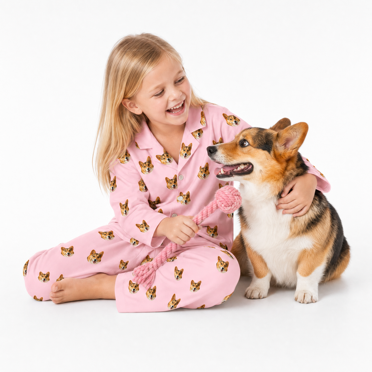 Child in pink pajamas with dog pattern playing with a dog on a white background