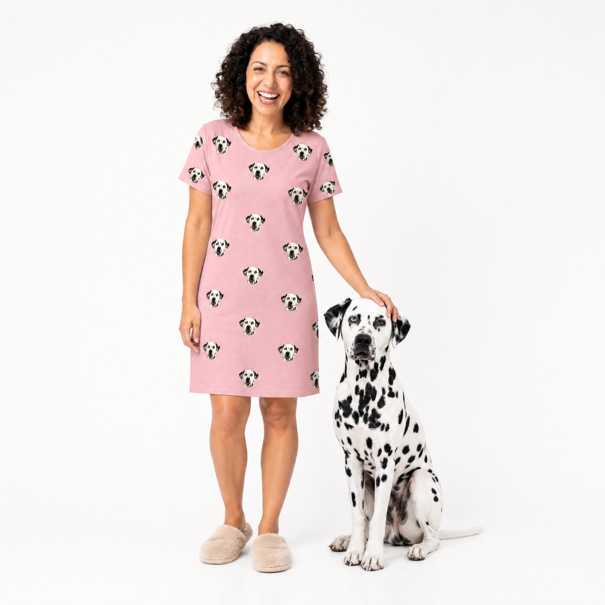 Woman wearing a pink nightgown with dog pattern standing next to a Dalmatian dog on a white background