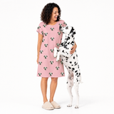 Woman wearing a pink nightgown with dog pattern, standing next to a Dalmatian dog on a white background