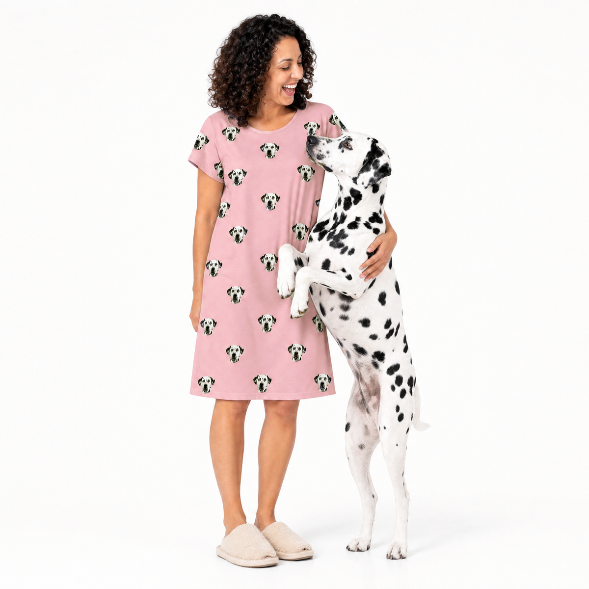 Woman wearing a pink nightgown with dog pattern, standing next to a Dalmatian dog on a white background