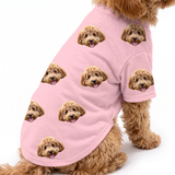 Dog wearing a pink custom dog shirt with a repeating dog face pattern on a white studio background.
