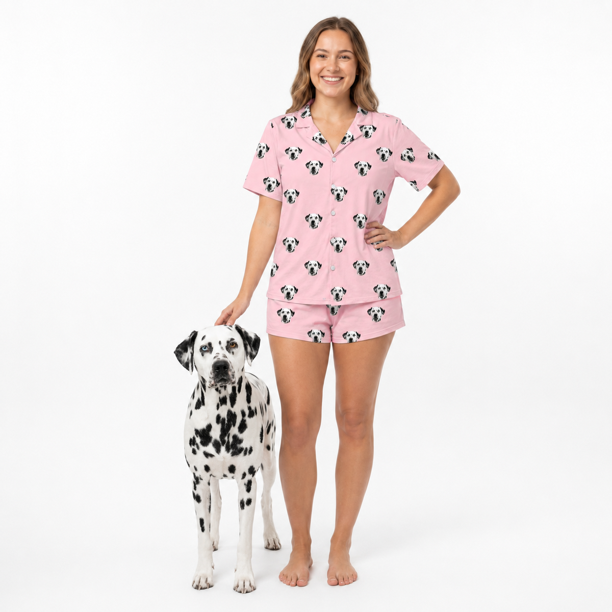 Woman wearing pink pajama set with dog pattern, standing next to a dalmatian dog on a white background