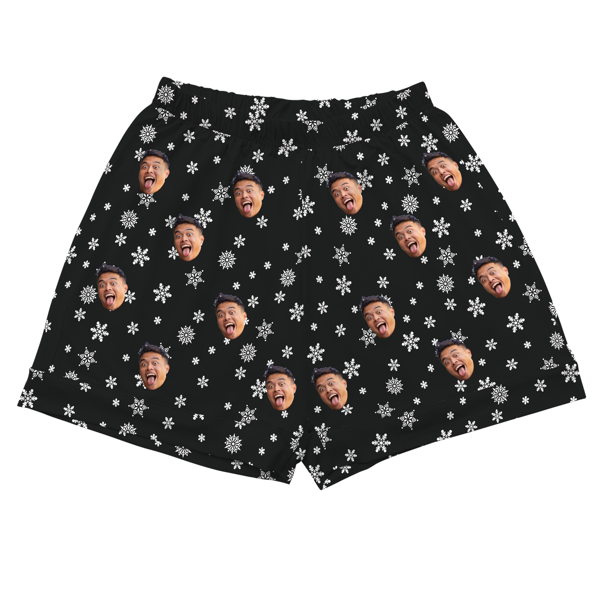 A pair of black athletic or pajama shorts with an elastic waistband. The fabric is patterned with small white snowflakes and repeated, highly expressive headshots of a person's face.