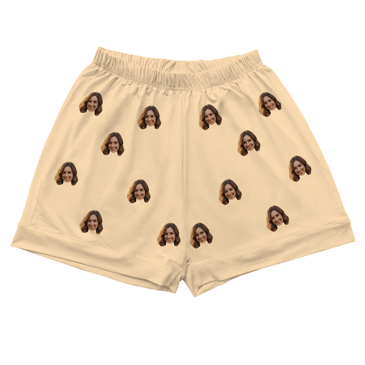 A pair of athletic or pajama shorts with a gathered, elastic waistband, made from a solid butter yellow or pale cream fabric. Repeated headshots of a smiling woman's face are evenly spaced and superimposed across the fabric.