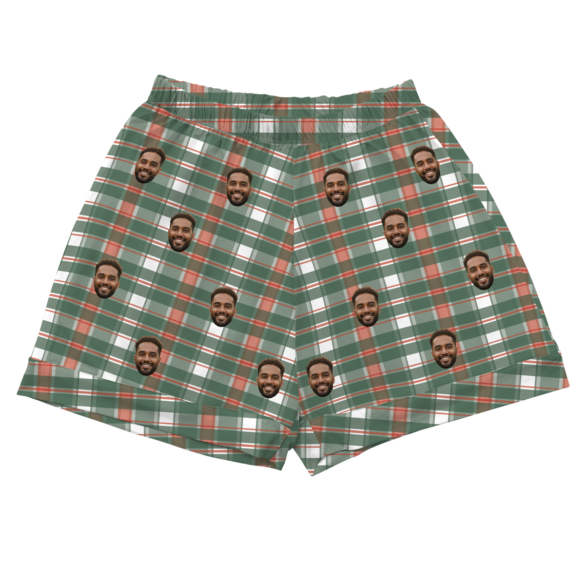 A pair of athletic or pajama shorts with an elastic waistband, featuring a plaid or flannel-style pattern in green, white, and red/rust colors. Repeated headshots of a smiling, bearded man are superimposed onto the plaid fabric.