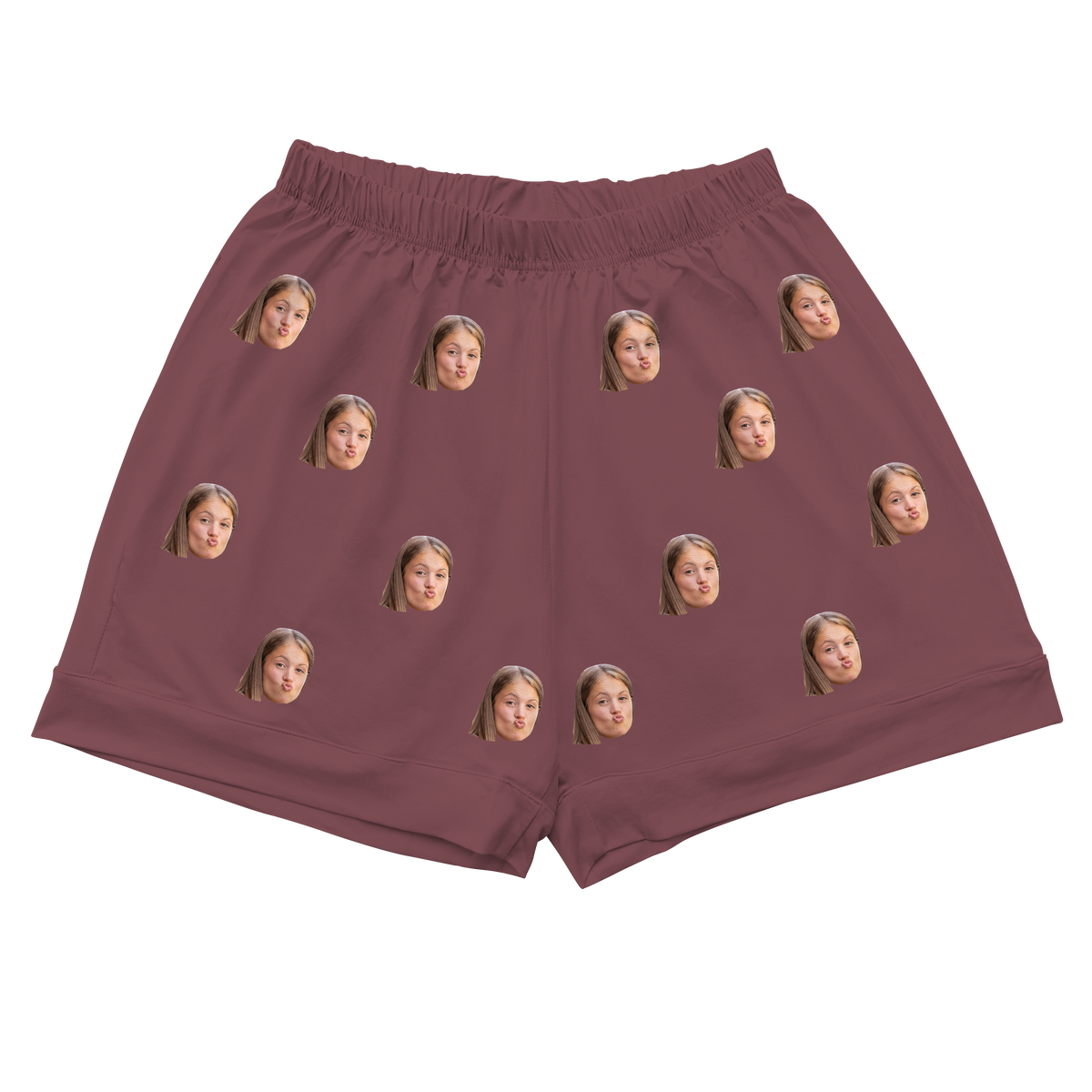 A pair of athletic or pajama shorts with a gathered, elastic waistband, made from a solid maroon or dusty rose-colored fabric. Repeated headshots of a young girl's face, making a playful 'fish face' or blowing a kiss, are evenly spaced and superimposed across the fabric. 
