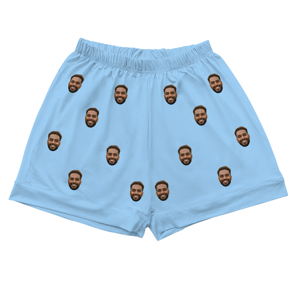 A pair of athletic or pajama shorts with a gathered, elastic waistband, made from a solid sky blue fabric. Repeated headshots of a smiling, bearded man's face are evenly spaced and superimposed across the fabric.
