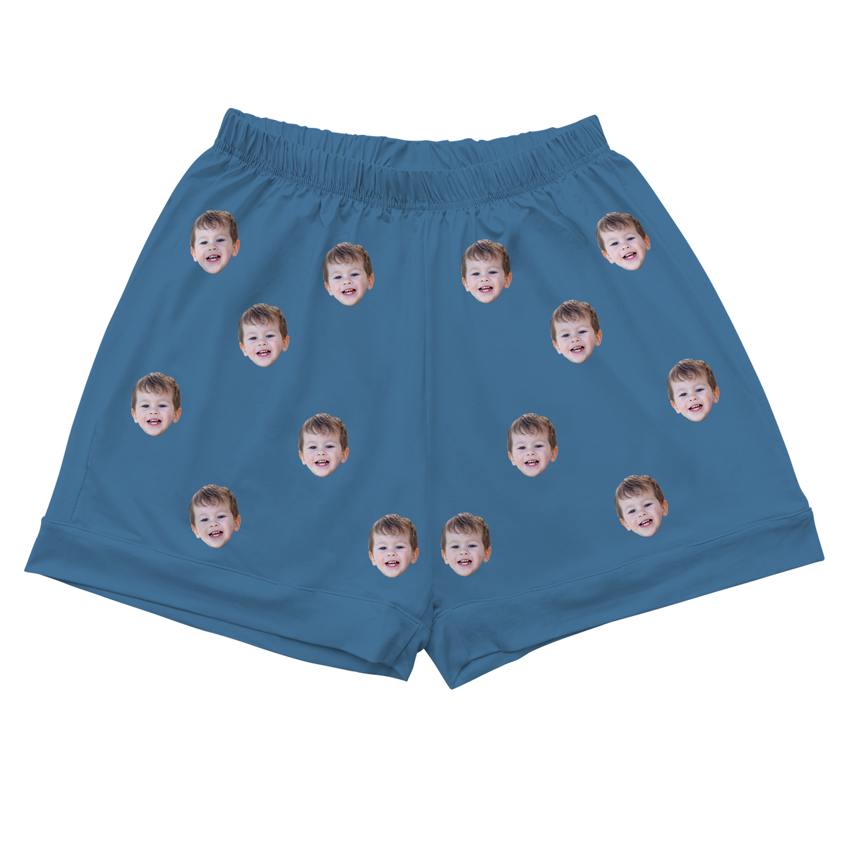 A pair of athletic or pajama shorts with an elastic waistband, made from a solid teal or dark turquoise fabric. Repeated headshots of a smiling woman's face are evenly spaced and superimposed across the fabric.
