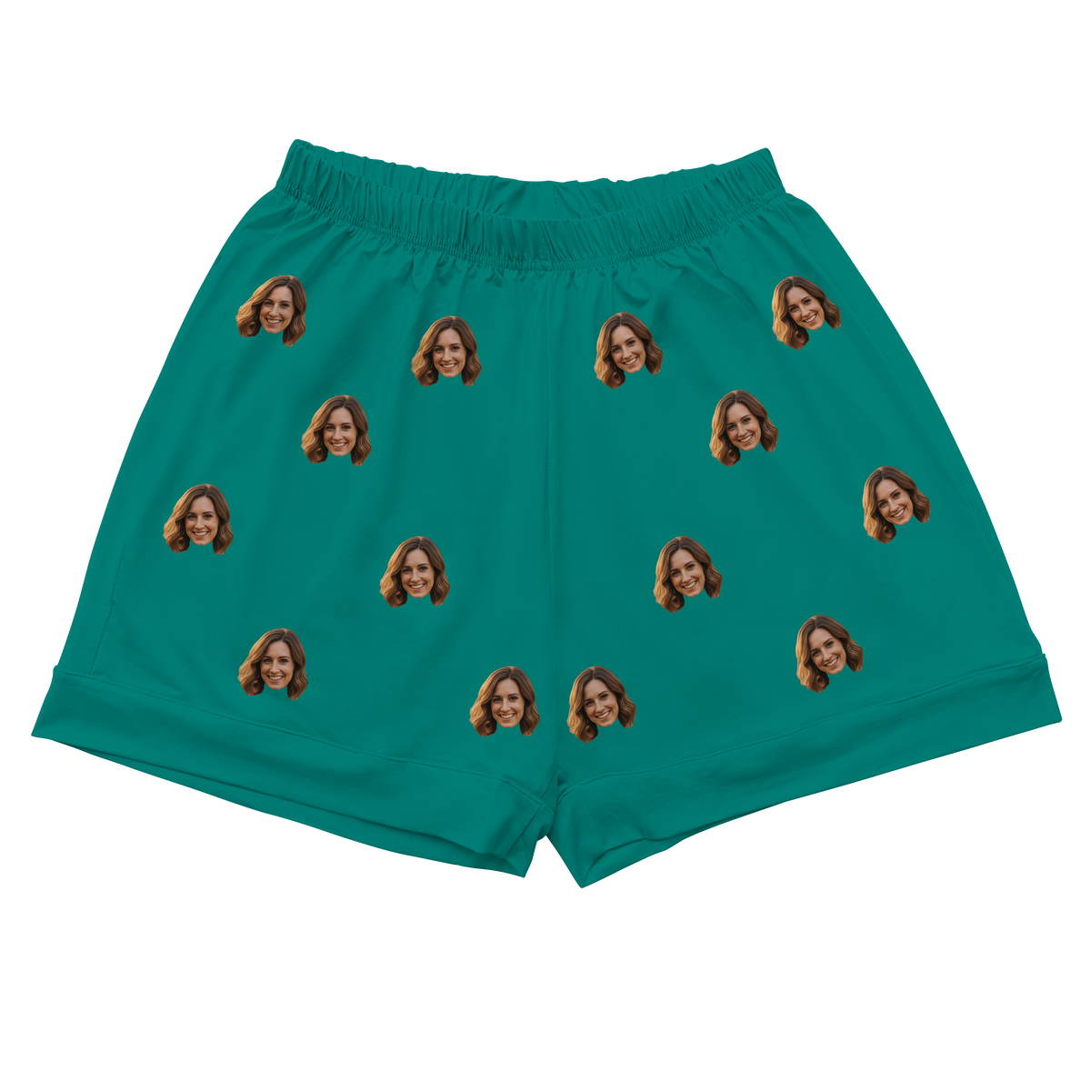 A pair of athletic or pajama shorts with an elastic waistband, made from a solid teal or dark turquoise fabric. Repeated headshots of a smiling woman's face are evenly spaced and superimposed across the fabric.