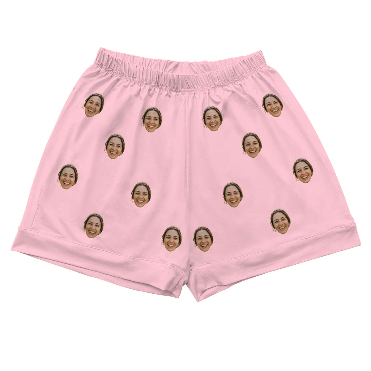 A pair pajama shorts with a gathered, elastic waistband, made from a solid light pink or blush-colored fabric. Repeated headshots of a smiling woman's face are evenly spaced and superimposed across the fabric.