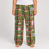 A person wearing green plaid pajama pants with dog face prints, pink bows, and small decorative graphics, shown from the waist down against a light gray studio background.