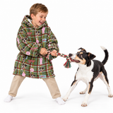 A child wearing a green plaid hooded robe with dog-themed prints is playfully tug-of-war with a black, white, and tan dog on a white studio background.