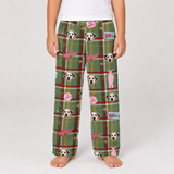 A child wearing green plaid pajama pants with a repeating pattern of Dalmatian dog faces, pink bows, and small pink-and-white cartoon figures, shown against a light gray studio background.