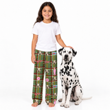 A young girl stands barefoot next to a Dalmatian dog on a white studio background, wearing green plaid pajama pants with a dog-themed pattern and a white t-shirt.