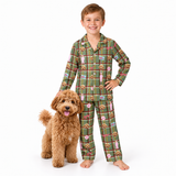 A young boy wearing green plaid pajamas with a dog print stands next to a fluffy brown dog on a solid white background.