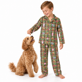 A young boy wearing green plaid pajamas with a dog print stands next to a fluffy golden dog on a white background, smiling as the boy offers a treat.
