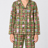 A person wearing a matching green plaid pajama set with cartoon dog faces, pink figures, and small blue-and-white signs, photographed against a light gray studio background.
