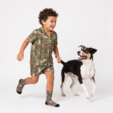 Young boy happily running next to a black, white, and tan dog, wearing green plaid short-sleeve pajamas and matching socks with custom dog face prints and pink bunny suit patterns.