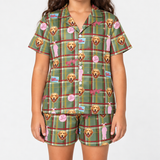 Close-up view of green plaid short-sleeve button-up pajama shirt and matching shorts, featuring Golden Retriever face prints and pink A Christmas Story bunny suit patterns.
