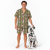 A man wearing a matching green plaid pajama set with a dog print stands next to a Dalmatian dog on a white studio background.