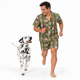 A man wearing a green plaid pajama set with a dog print is jogging barefoot next to a Dalmatian dog on a white studio background.