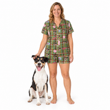 A woman wearing a green plaid pajama set with a dog print stands barefoot next to a black, white, and tan dog on a solid white background.