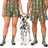A man and a woman wearing matching green plaid pajama sets with a Dalmatian dog standing in the center. The pajamas feature a repeating pattern of Dalmatian dog faces, pink heart-shaped balloons, and small novelty signs.