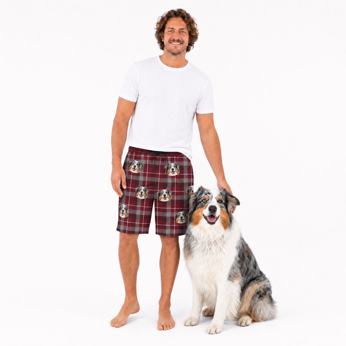 Man wearing plaid shorts with dog pattern standing next to a dog on a white background
