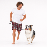 Man walking a dog wearing plaid shorts with dog pattern, on a white background