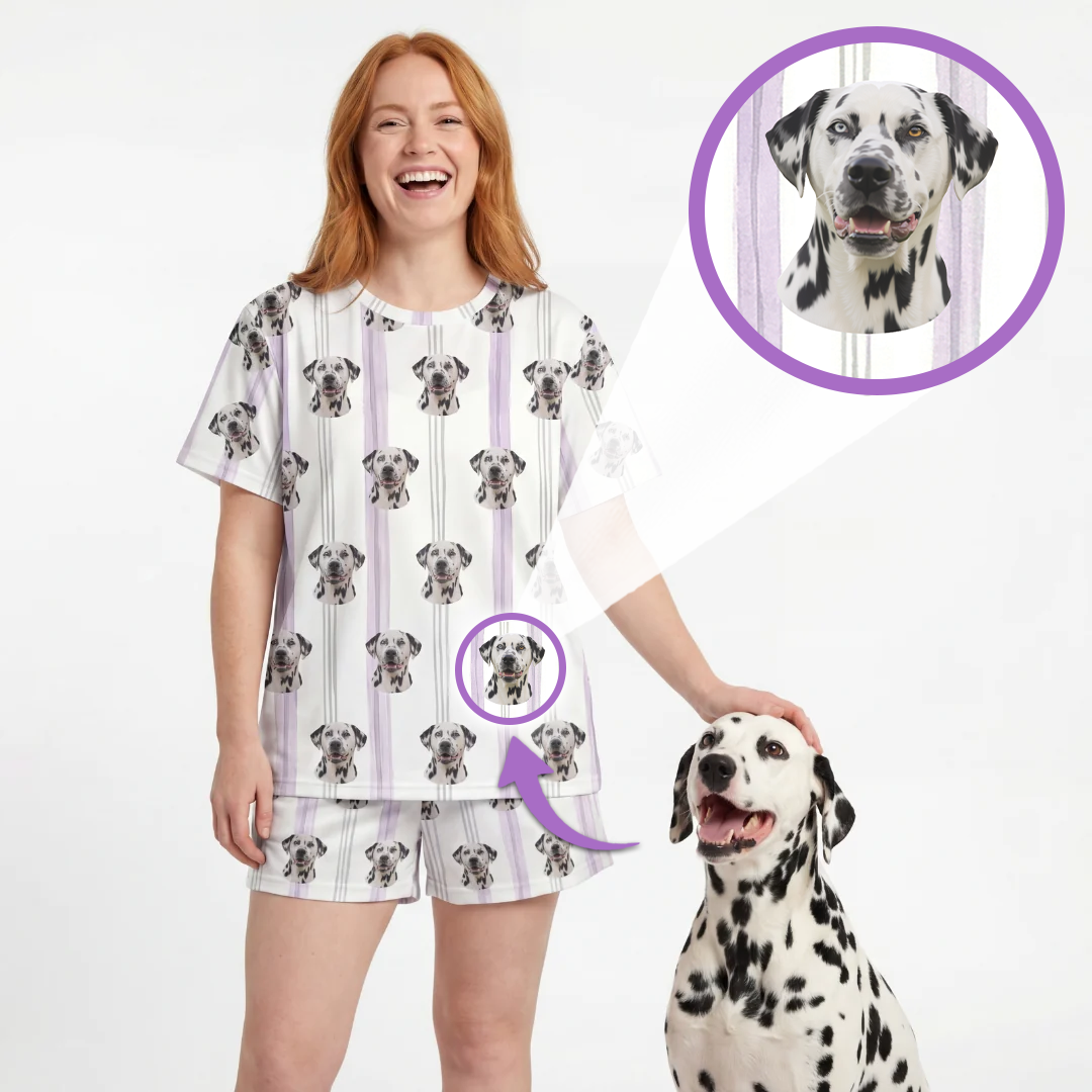 A woman wearing a matching short-sleeve pajama top and shorts set with a Dalmatian dog print, standing next to a Dalmatian dog. The pajamas feature a white base with vertical lavender stripes and a repeating pattern of the dog's face.