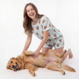 Woman in patterned pajamas playing with a golden retriever on a white background