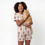 Woman wearing a cat-themed pajama set holding a cat on a white background [TerracottaStripes]