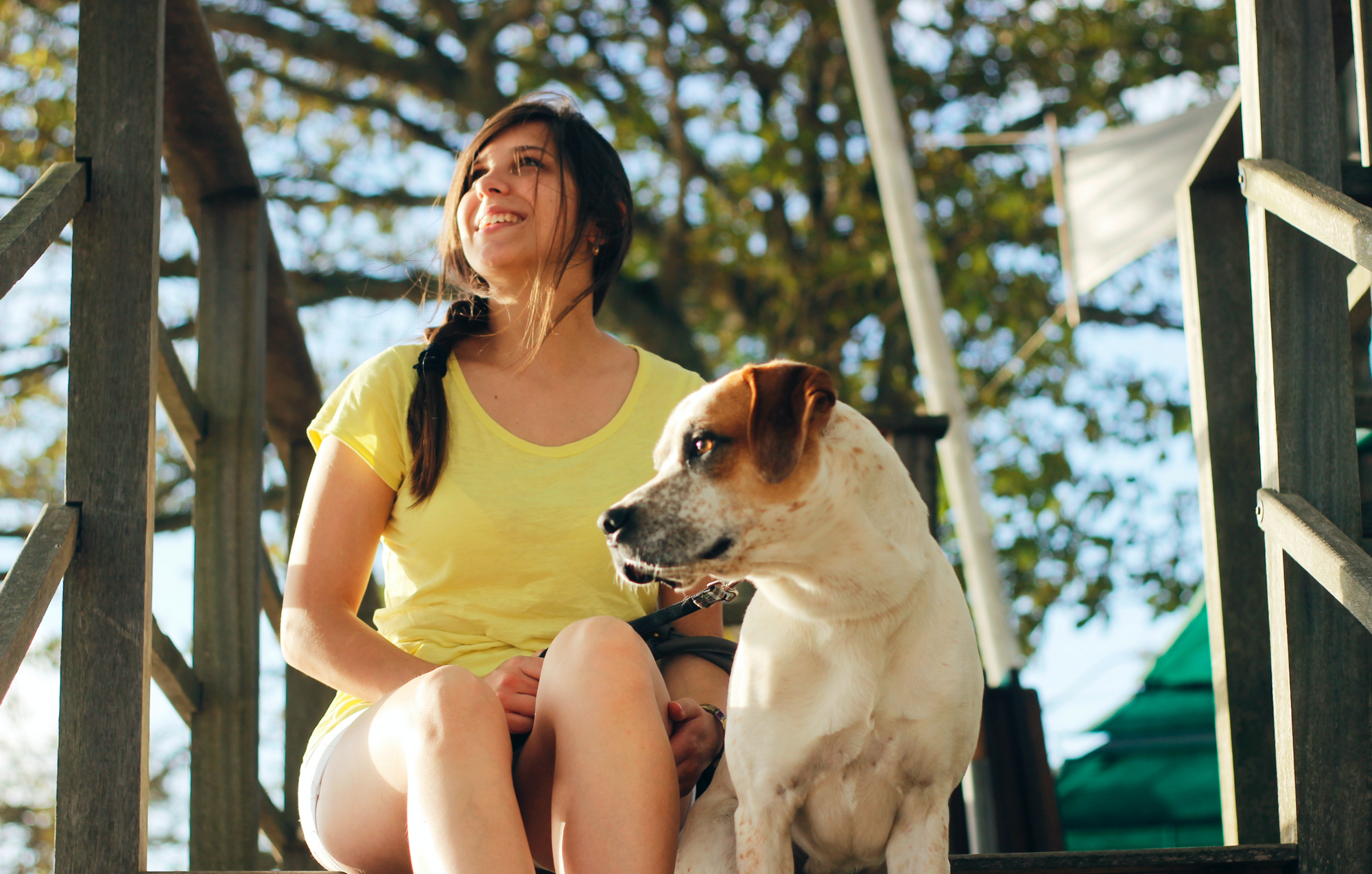 Woman in a yellow shirt sitting on a porch with her dog.