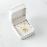 Gold dog-portrait pendant in a white velvet jewelry box on a marble surface.