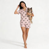 Woman wearing pink pajama set with dog pattern, holding a small dog, on a white background
