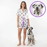 Woman wearing custom short-sleeve button-down pajama set in lilac stripes printed with her Dalmatian's face, standing next to her dog.