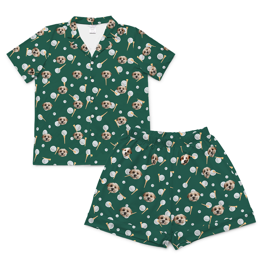 A matching short-sleeve pajama set (top and shorts) rendered in a dark green fabric. The entire set is covered in a repeating golf-themed pattern featuring alternating elements: white golf balls, light yellow golf tees, and smiling headshots of a dog.