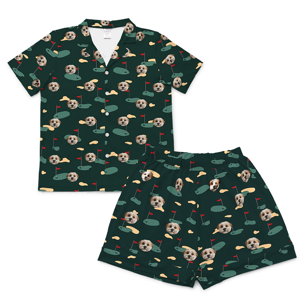 A matching short-sleeve pajama set (top and shorts) rendered in a dark green fabric. The entire set is covered in a repeating golf-themed pattern featuring alternating elements: cartoon depictions of golf putting greens with a red flag, yellowish sand traps, and smiling headshots of a dog.