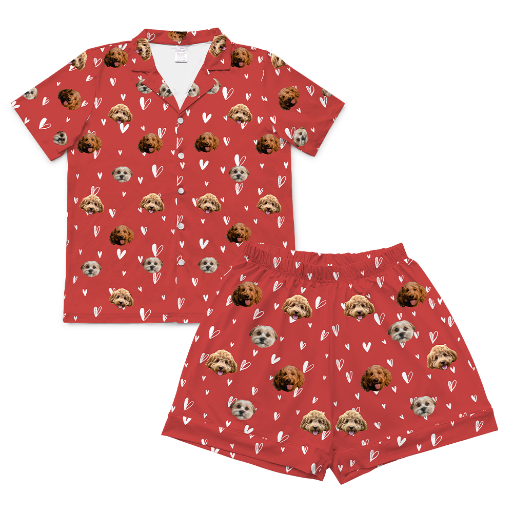 A set of short-sleeve pajamas in a vibrant red color. The fabric is patterned with small, white, hand-drawn outline hearts. The main motif is a repeating pattern of small, cropped photos of three different dogs' faces.