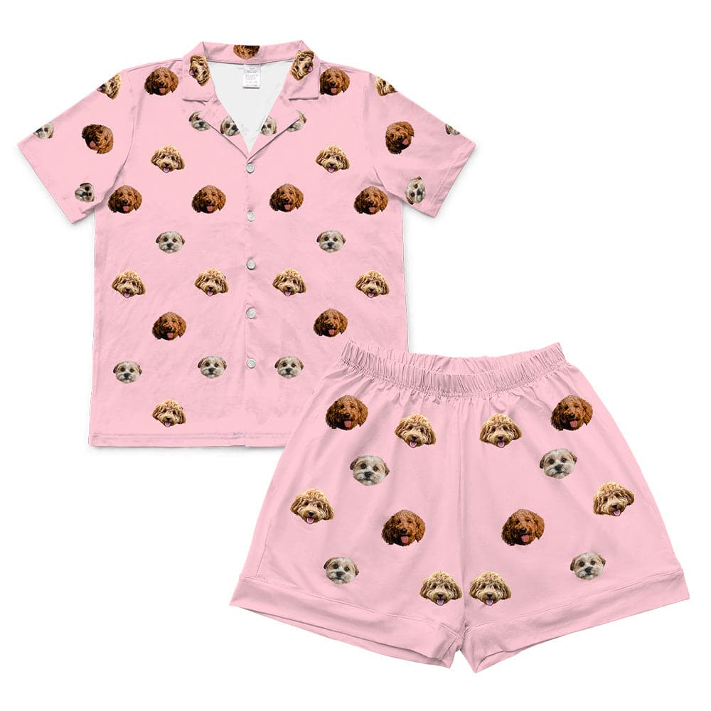 Pink pajama shorts with elastic waistband and rolled cuffs, featuring a scattered print pattern of realistic doodle dog faces in brown, tan, and cream colors.