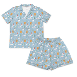 A two-piece pajama set featuring a short-sleeve button-up shirt and matching shorts in light blue, both printed with a whimsical pattern of cartoon bears, snowmobiles, evergreen trees, and snowflakes.