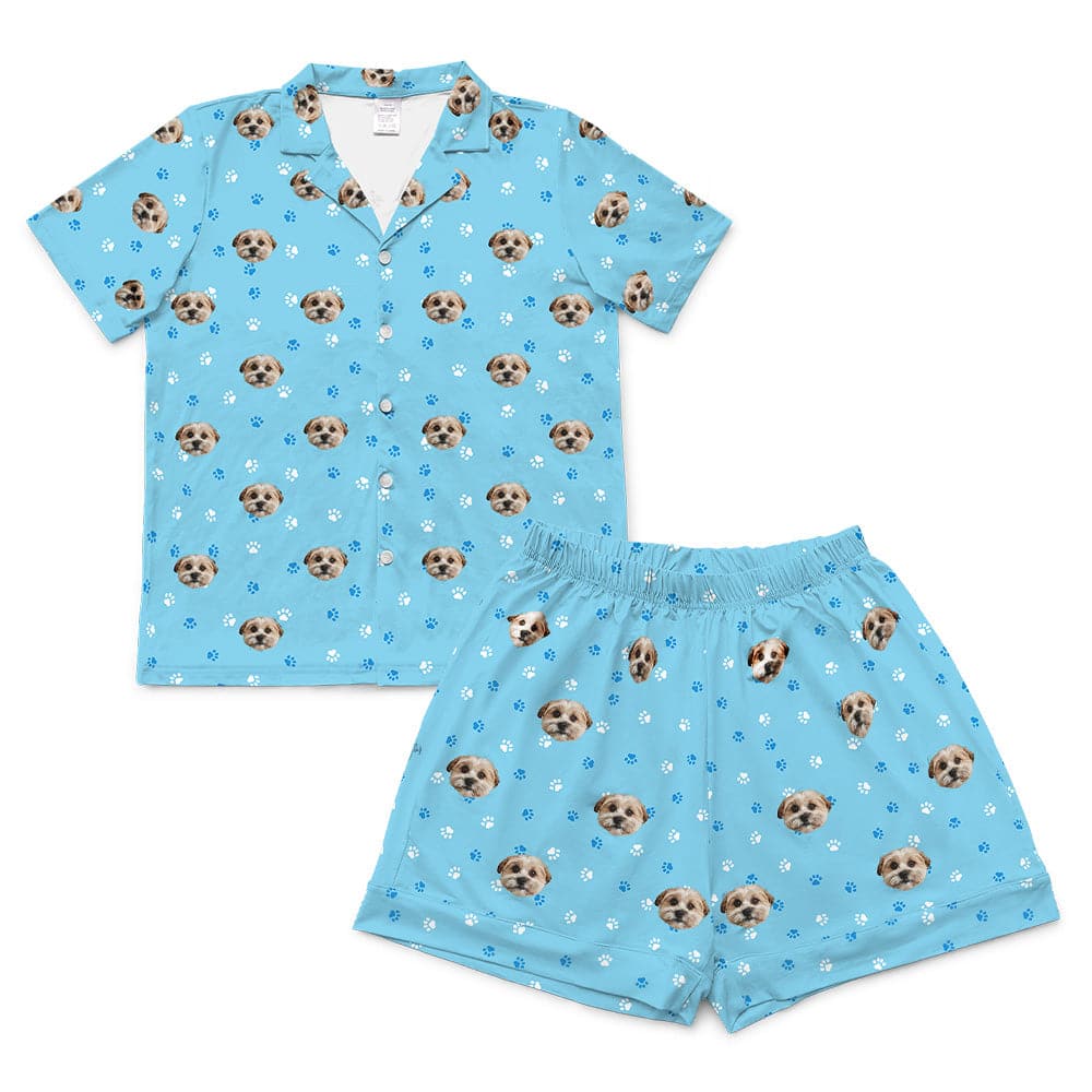 Light blue short-sleeve pajama set, including a button-down top and matching shorts, both patterned with dog faces and white and dark blue paw prints.