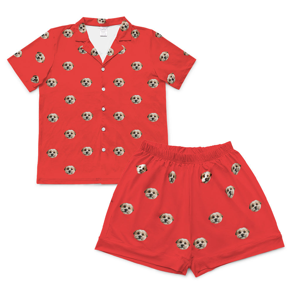 A matching short-sleeve pajama set (shirt and shorts) in a solid vibrant red color. The fabric is covered in a repeating, all-over pattern of small, cropped dog faces.