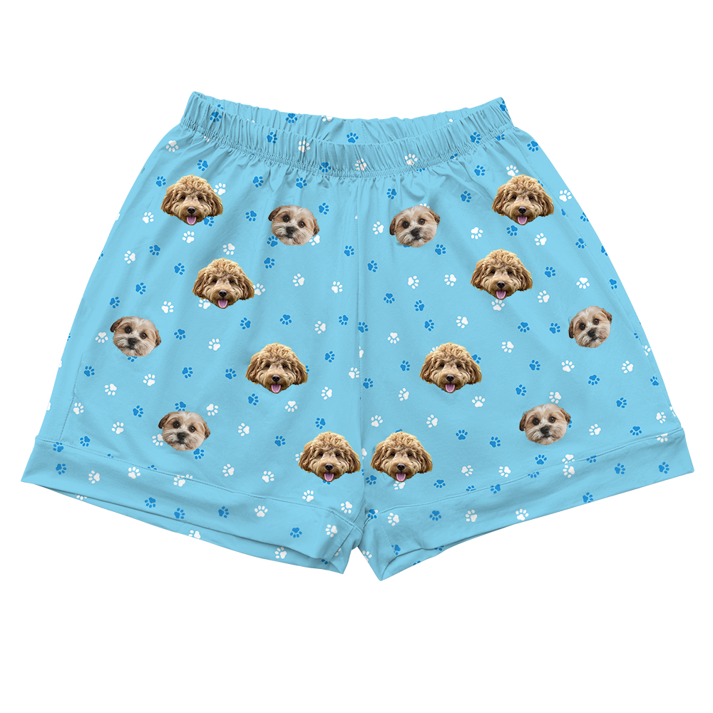 Light blue pajama shorts featuring an all-over pattern of two different small dog faces and scattered blue and white paw prints.