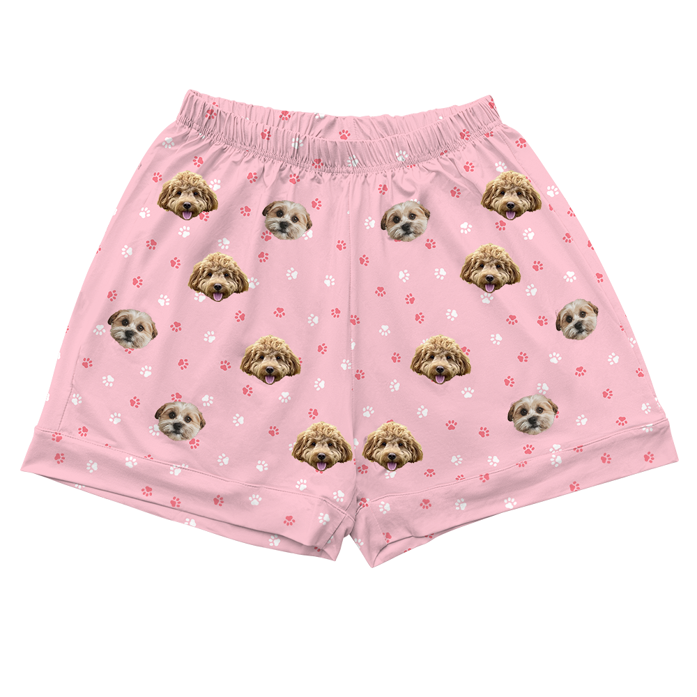 Pink pajama shorts decorated with two different dog faces and scattered white and pink paw prints.