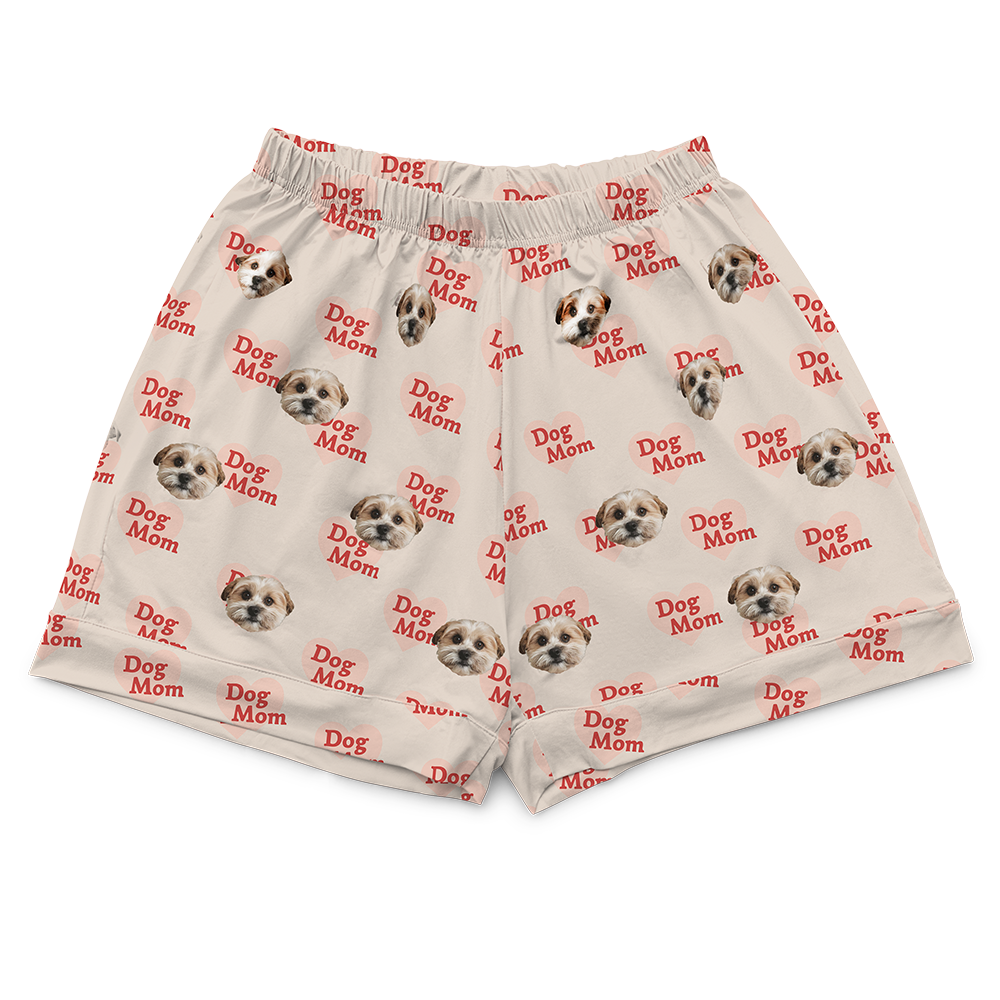 Beige pajama shorts (part of a short-sleeve set) with an elasticated waist. The shorts are covered in a repeating pattern featuring alternating elements: pink heart shapes with the red text "Dog Mom" inside, and smiling headshots of a dog.