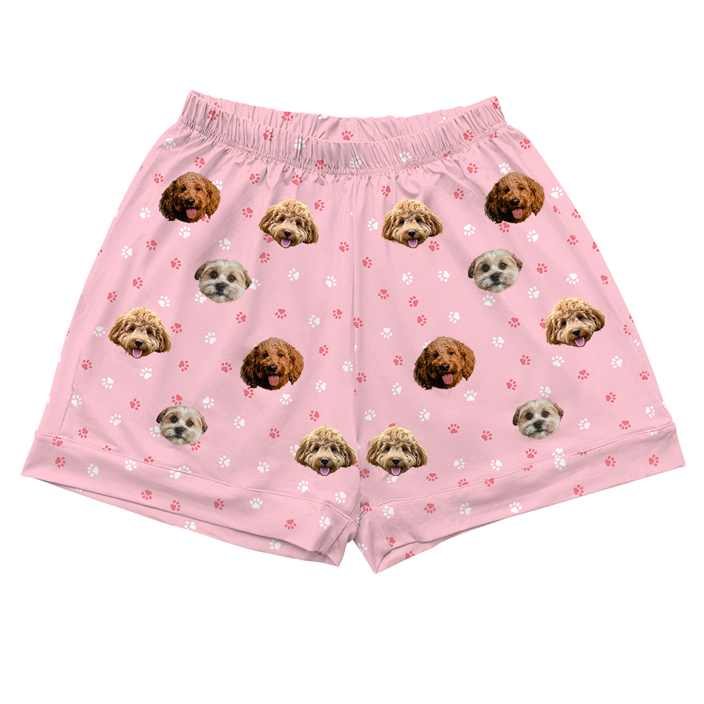 Pink pajama shorts featuring an all-over pattern of three different dog faces with scattered white and pink paw prints.