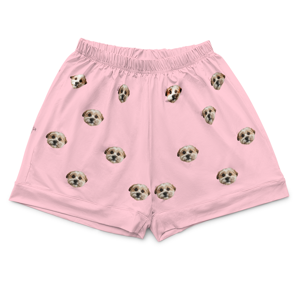 Close-up of a pair of light pink pajama shorts with an elastic waistband, featuring an all-over repeating pattern of a small dog's face.