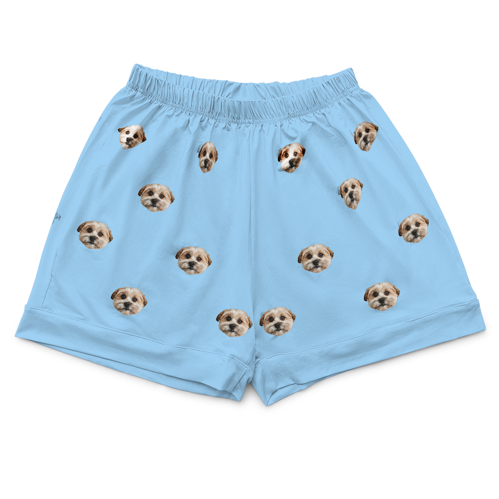 A pair of light sky blue pajama shorts. The shorts feature a repeating pattern of realistic photos of three different small dogs' heads.